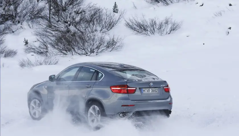 Szary BMW E71 X6 z napędem na cztery koła pokonuje zaspy śnieżne, unosząc chmury białego puchu.