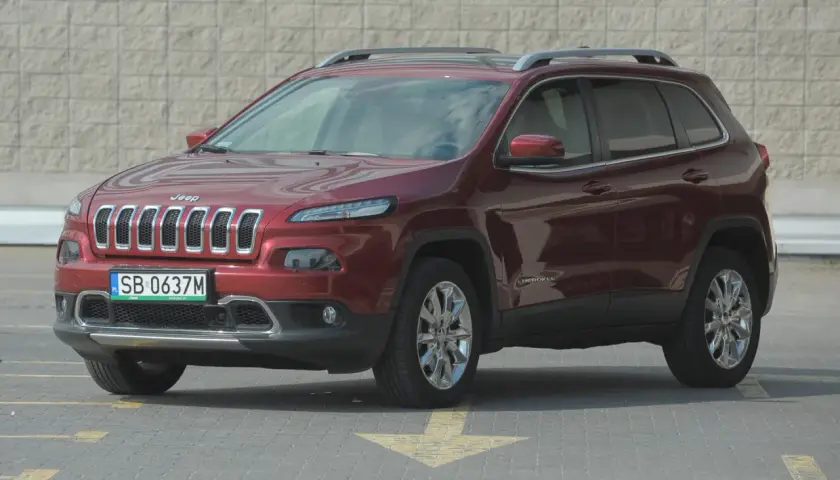 Czerwony Jeep Cherokee KL z polskimi tablicami rejestracyjnymi stoi na parkingu.