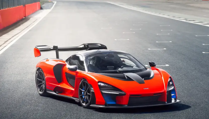 Pomarańczowy McLaren Senna z czarnym spojlerem i detalami na torze wyścigowym.