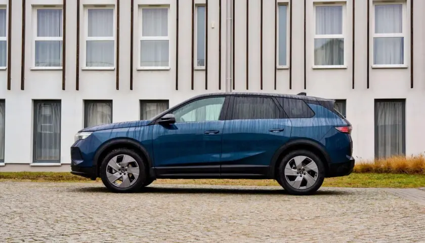Nowoczesny, granatowy Opel hybryda stoi na brukowanym podjeździe przed minimalistycznym budynkiem.