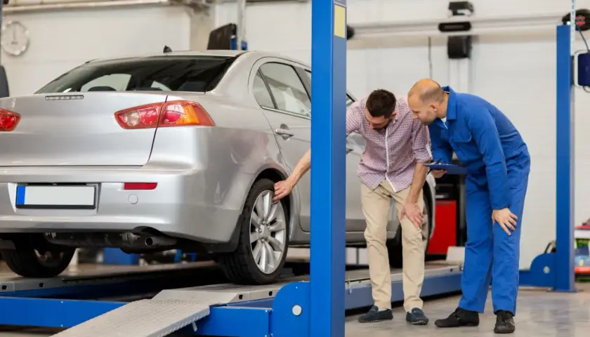 Mechanik i klient oglądają podniesiony samochód na podnośniku w warsztacie.