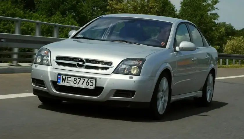 Srebrny Opel Vectra C GTS z polskimi tablicami WE 87765 jedzie po drodze, otoczony zielenią.