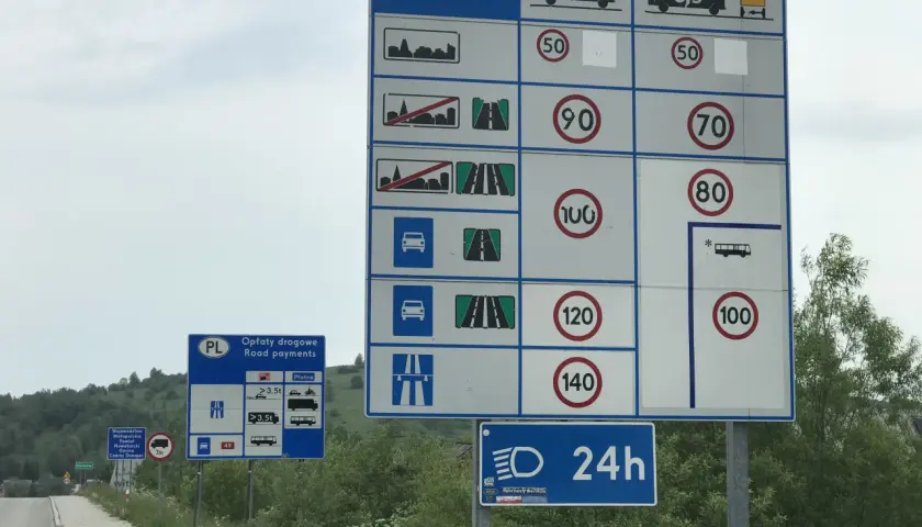 Znaki drogowe z limitami prędkości i informacją o opłatach drogowych na drodze ekspresowej.