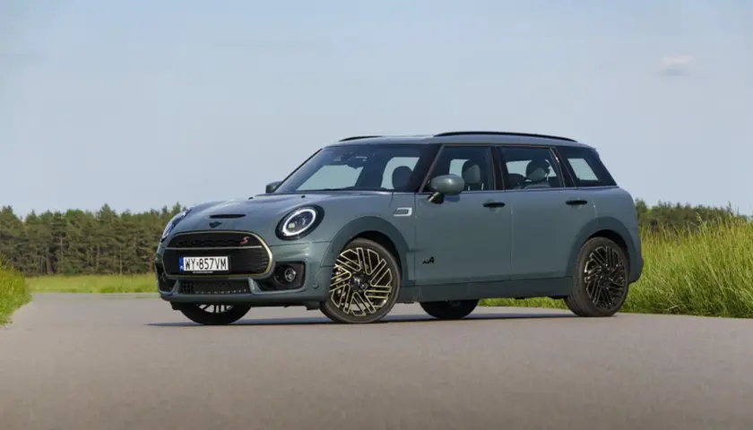 Szary Mini Clubman F54 z napędem ALL4 na tle lasu i łąki.