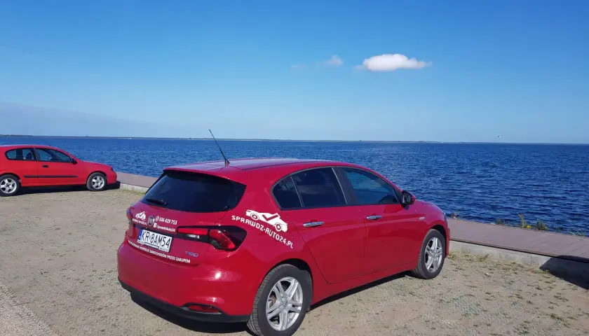 Czerwony fiat tipo sedan zaparkowany nad błękitnym jeziorem.