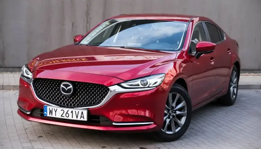 Czerwona Mazda 6 2.0 benzyna zaparkowana na kostce brukowej. Elegancka linia nadwozia i charakterystyczny grill.