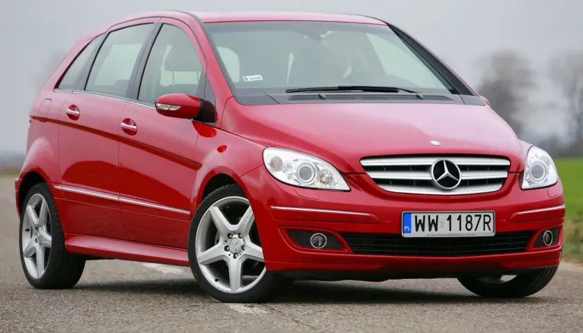 Czerwony Mercedes W245 na drodze, z widocznym grillem i reflektorami.