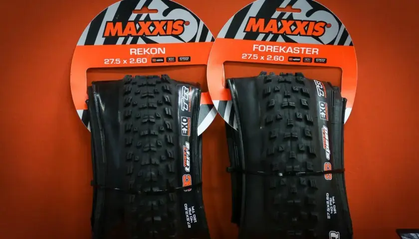 Dwie opony rowerowe Maxxis Rekon i Forekaster 27.5 x 2.60 na pomarańczowym tle.