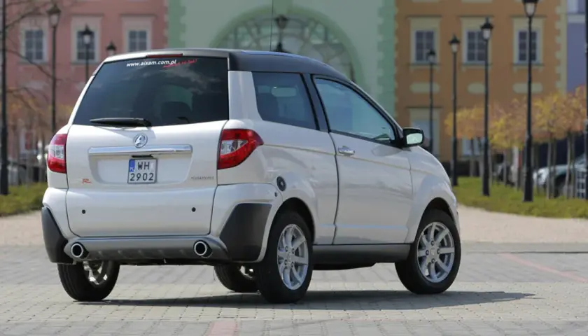 Białe auto Aixam GTR, idealne jako auto bez prawka, parkuje na brukowanym placu przed kolorowymi kamienicami.