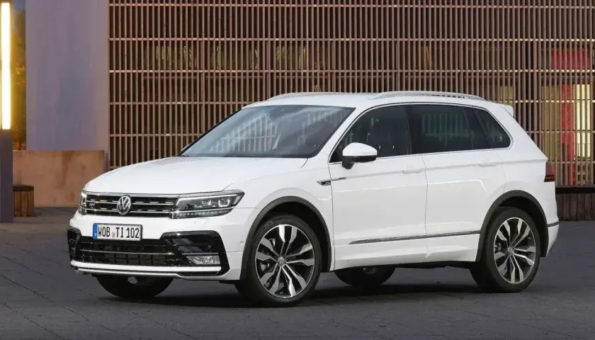 Biały Volkswagen Tiguan 5N z przyciemnianymi szybami i chromowanymi listwami, zaparkowany przed nowoczesnym budynkiem.