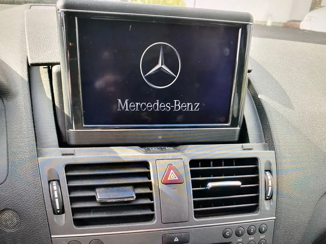 Wyświetlacz w samochodzie Mercedes-Benz z logo i napisem. Obok kratka nawiewu. Model w104.