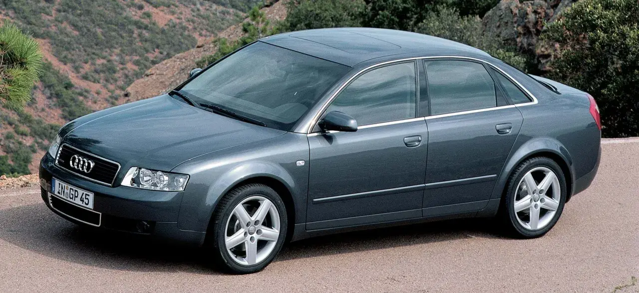 Szary sedan Audi A4 B6, produkowany w latach 2000-2006, parkuje na tle górskiego krajobrazu.