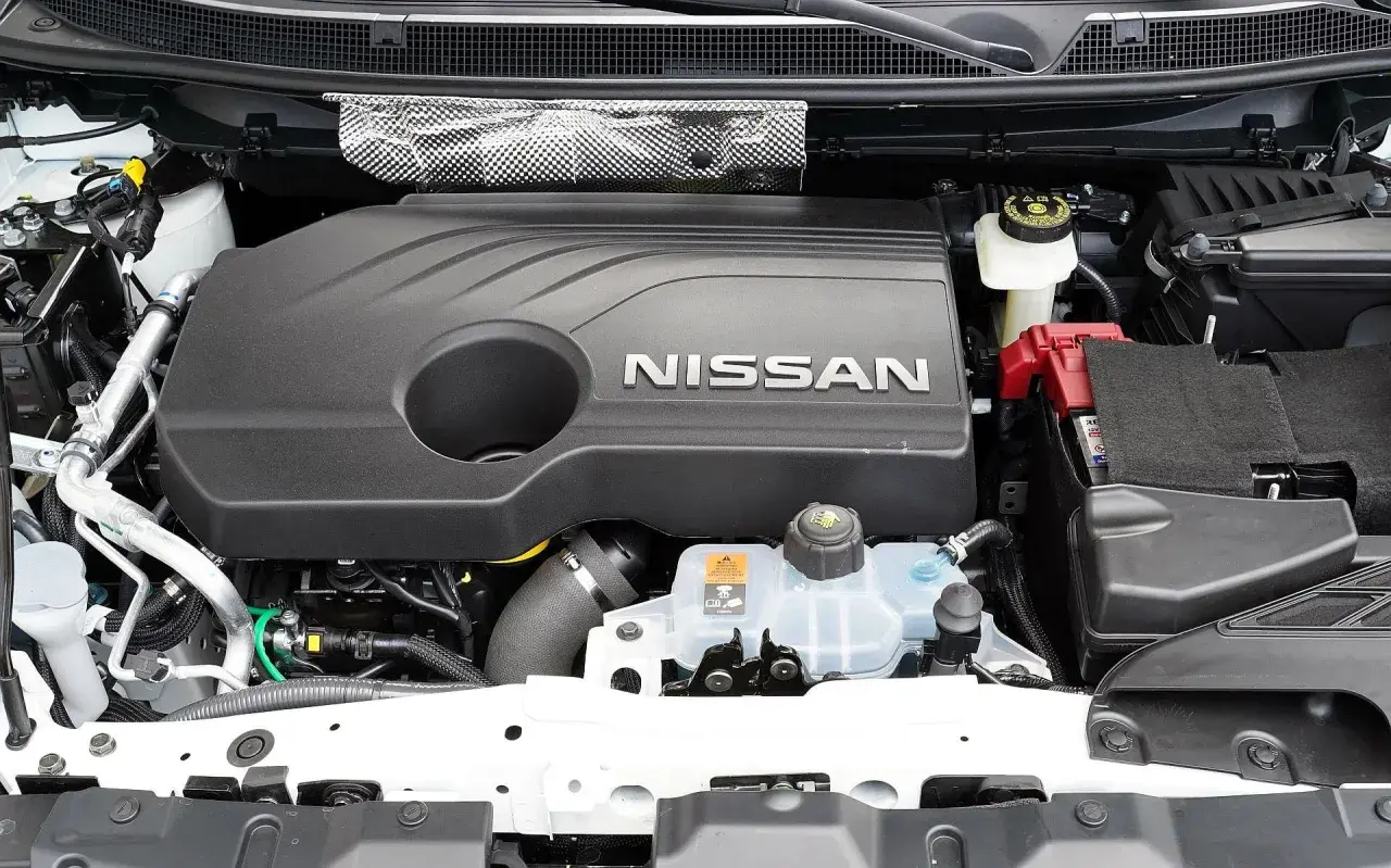 Silnik Nissana Qashqai J11, z widocznym napisem NISSAN na czarnej osłonie. Widać akumulator i zbiornik płynu chłodniczego.