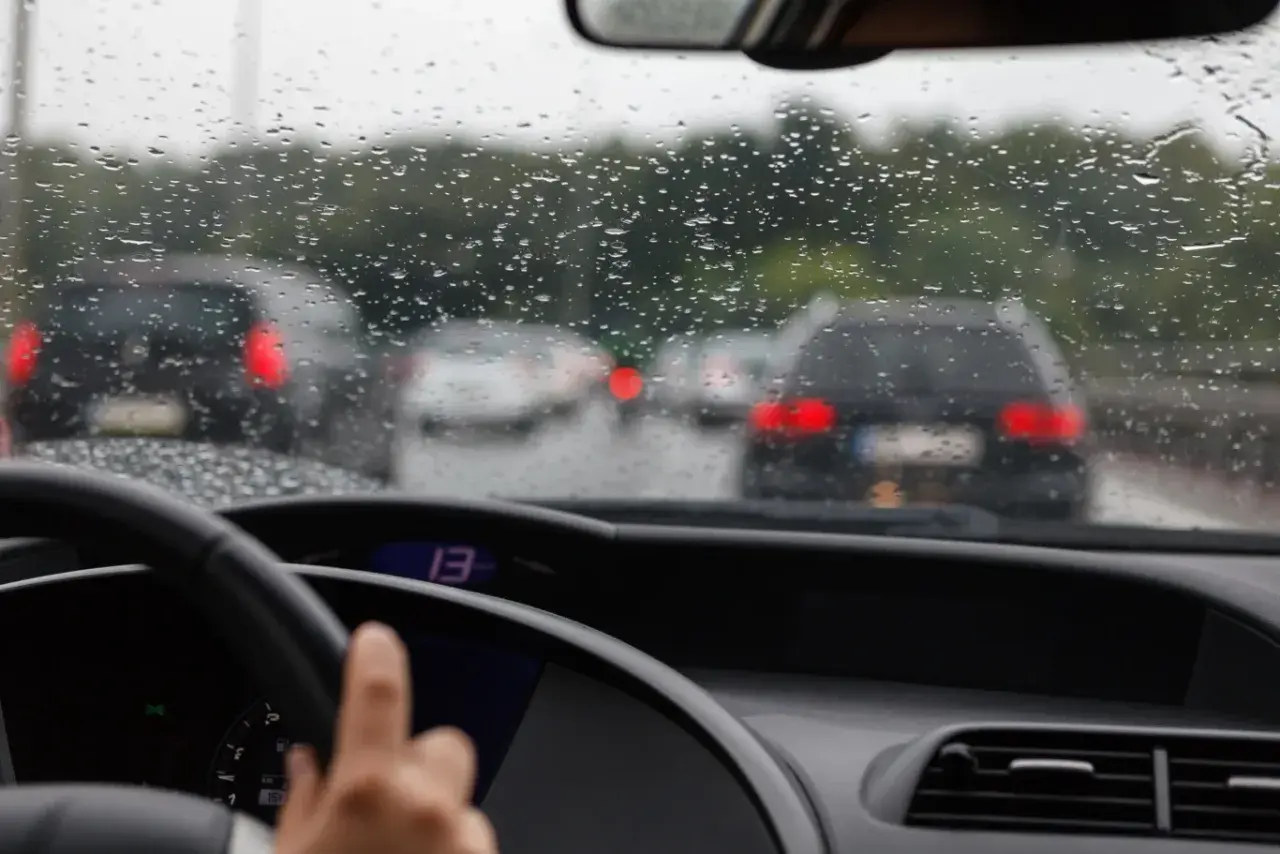 Widok z wnętrza samochodu na deszczową drogę z innymi autami i kroplami na szybie.