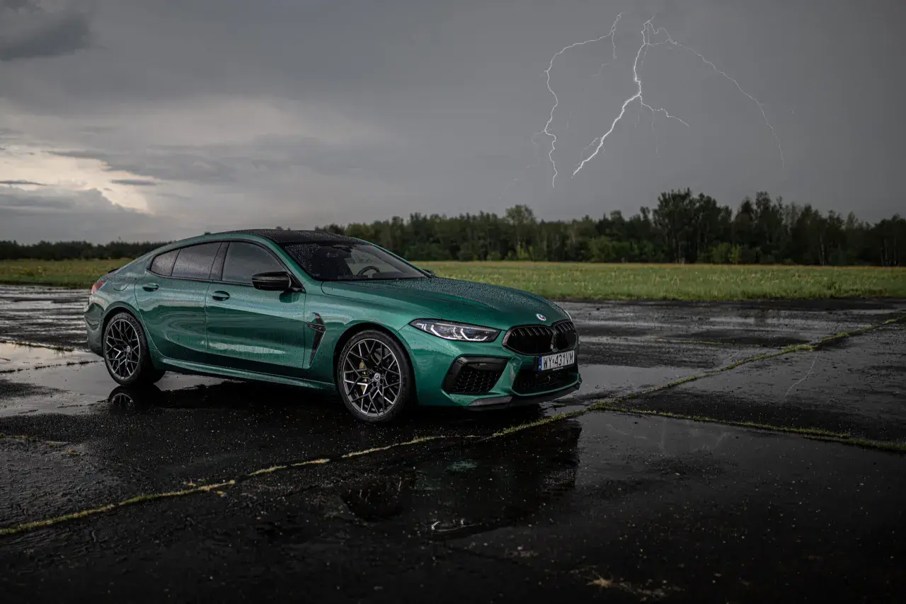 Zielony BMW M8 Competition Gran Coupé na mokrym asfalcie, z błyskawicą na burzowym niebie.