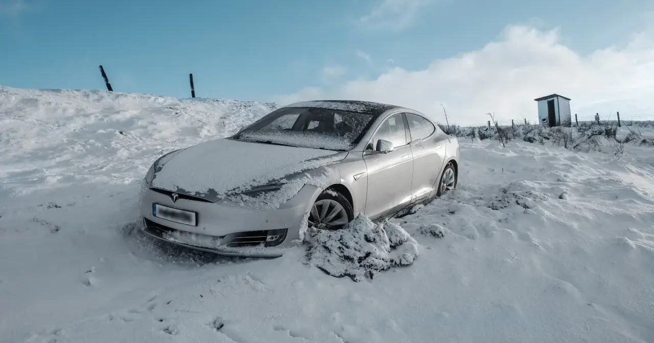 Srebrny samochód Tesla w śniegu, z widocznym logo marki.