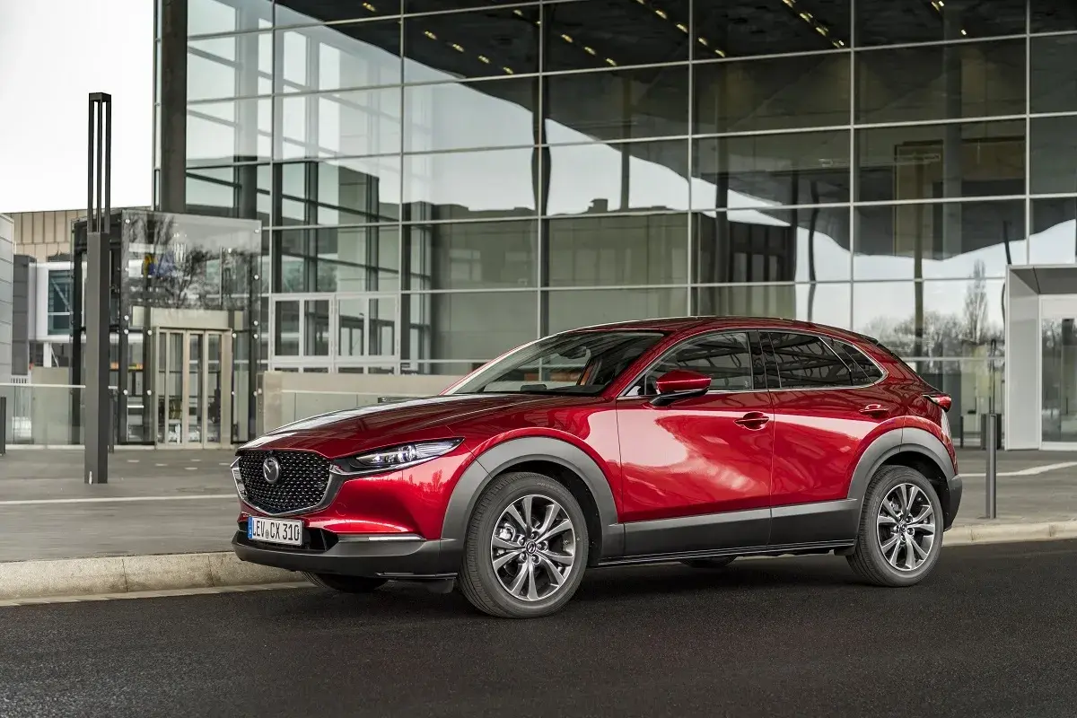 Czerwona Mazda CX-30 lśni przed nowoczesnym budynkiem z przeszkloną fasadą.