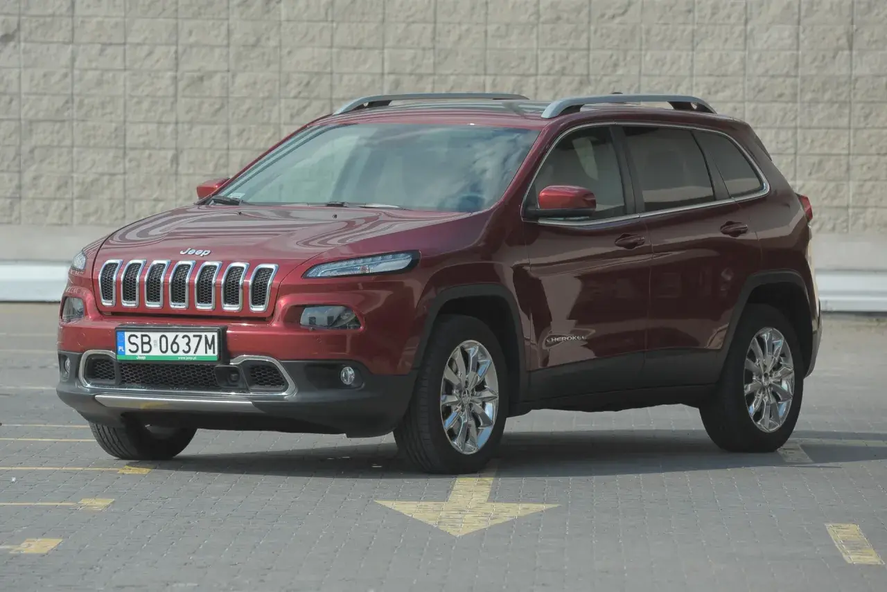 Czerwony Jeep Cherokee KL z polskimi tablicami rejestracyjnymi stoi na parkingu.