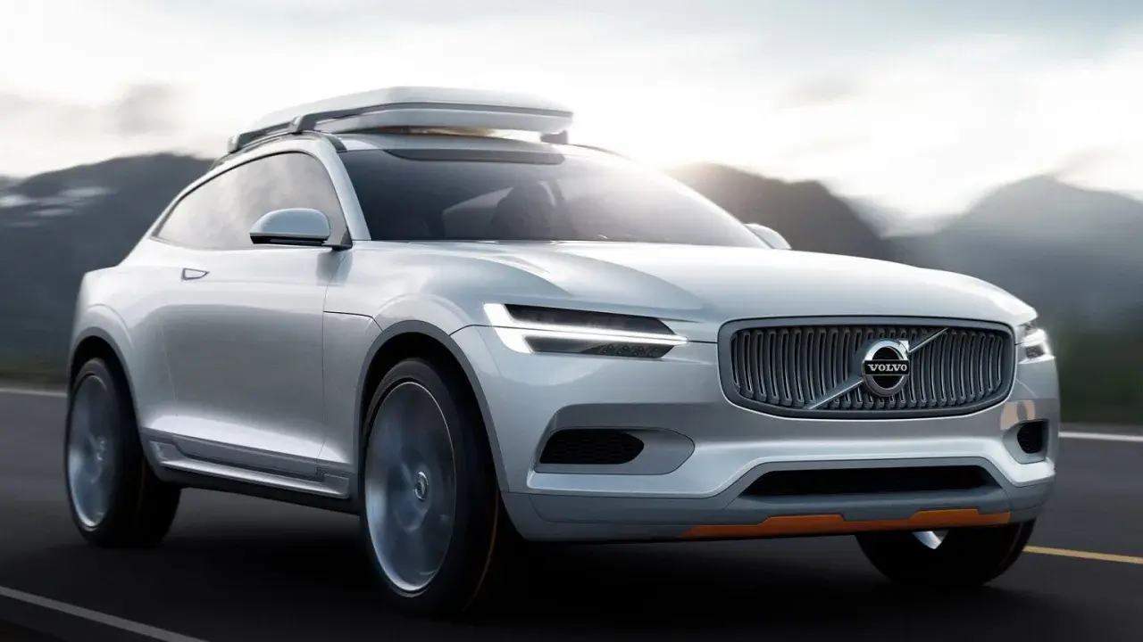 Biały Volvo XC100 z bagażnikiem dachowym jedzie po drodze, otoczony górami.