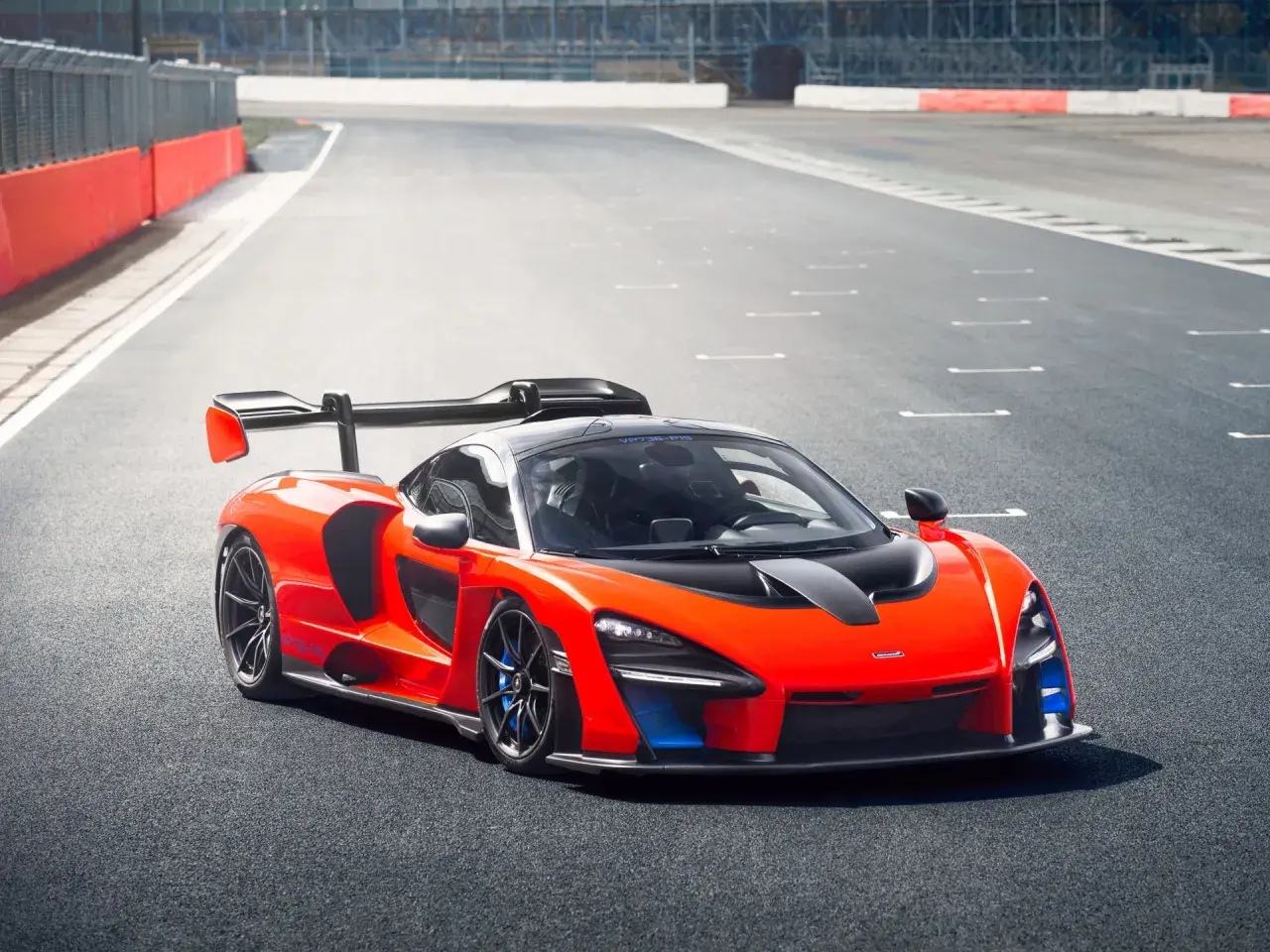 Pomarańczowy McLaren Senna z czarnym spojlerem i detalami na torze wyścigowym.