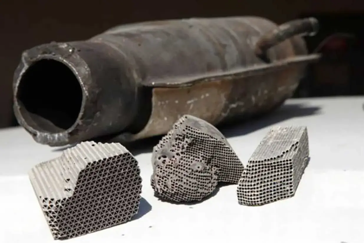 Rozcięty katalizator samochodowy z widocznym wkładem ceramicznym o strukturze plastra miodu.