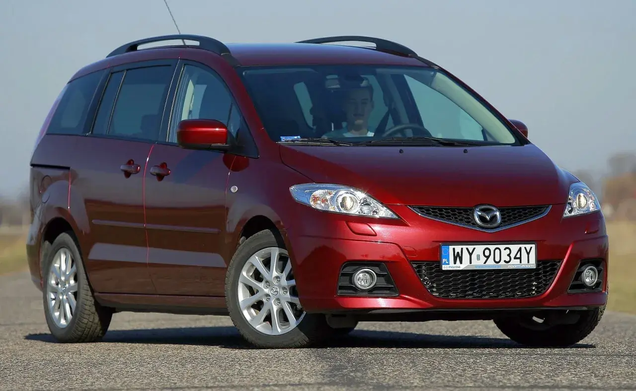Czerwona Mazda 5 CR z młodym kierowcą za kierownicą, zaparkowana na drodze.