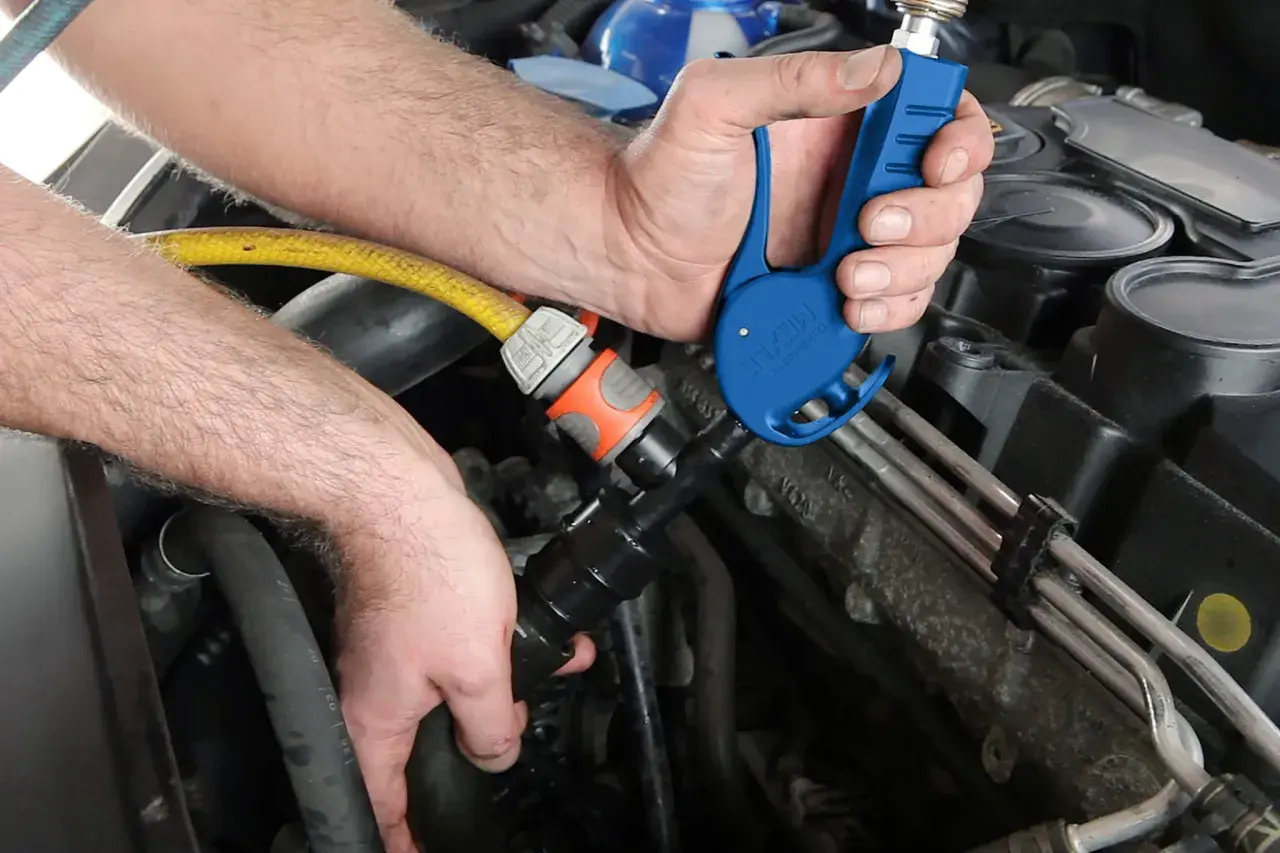 Ręce mechanika podłączają żółty wąż do niebieskiego narzędzia przy silniku samochodu.