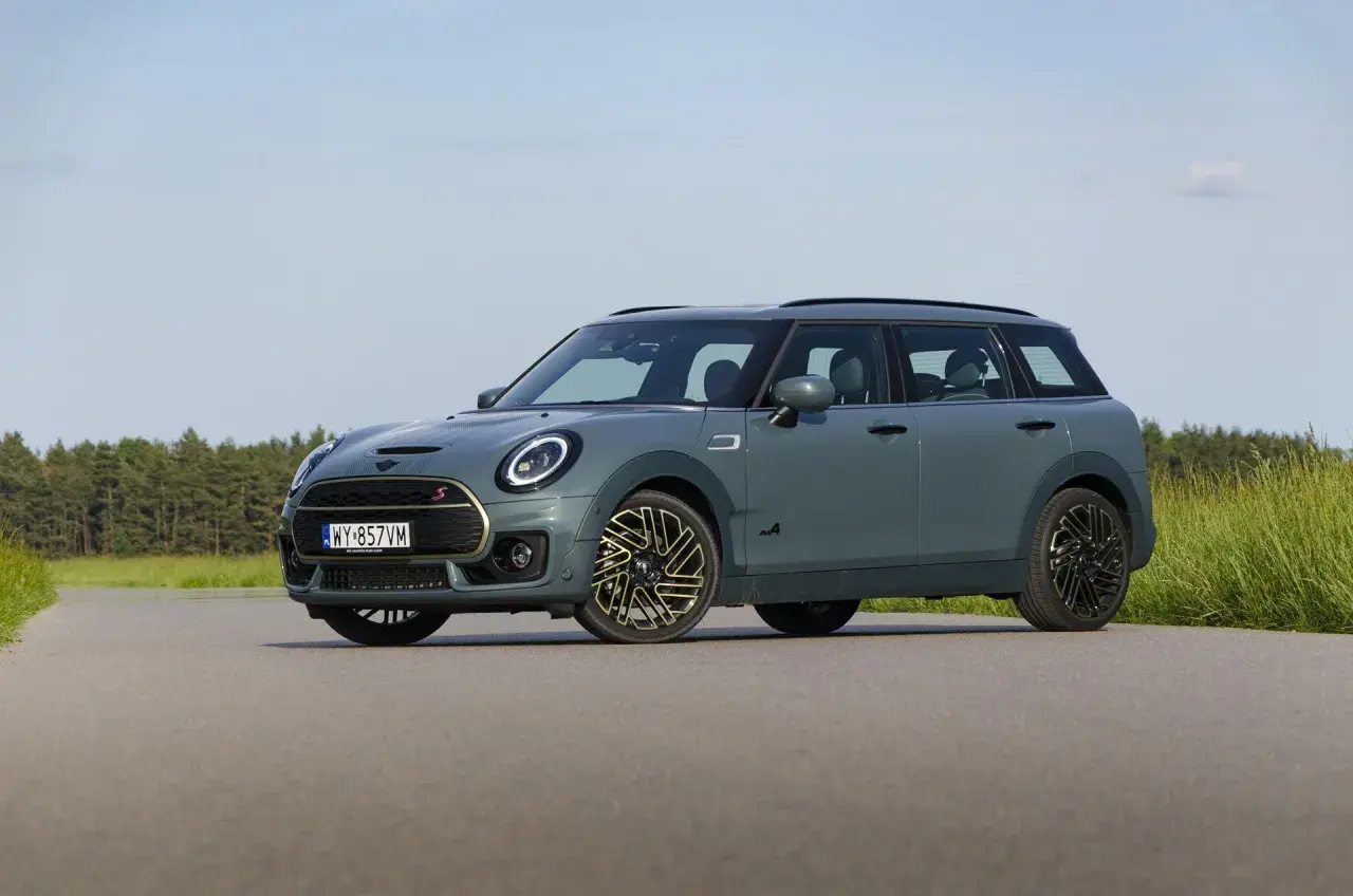 Szary Mini Clubman F54 z napędem ALL4 na tle lasu i łąki.