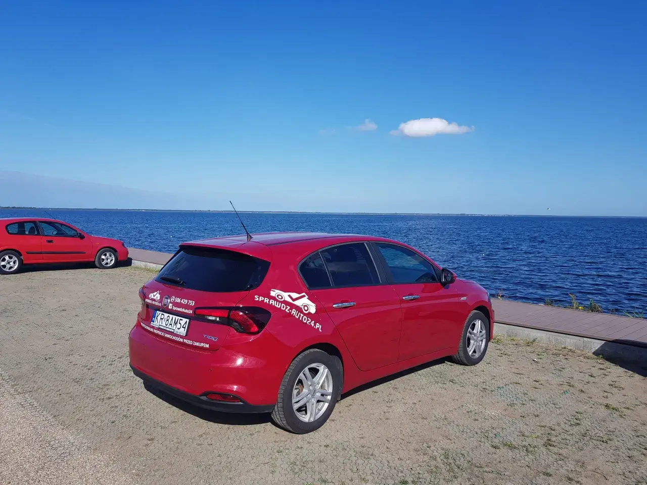 Czerwony fiat tipo sedan zaparkowany nad błękitnym jeziorem.