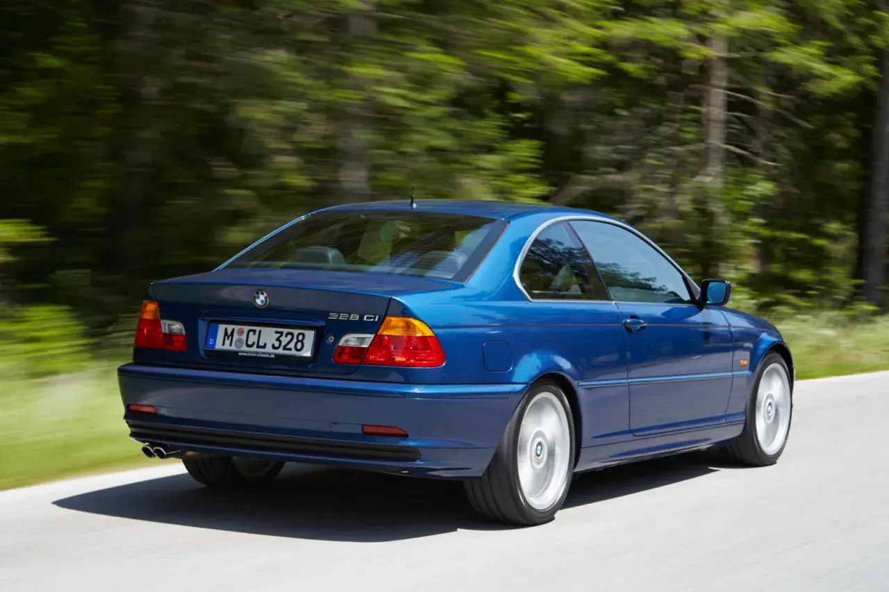 Niebieskie BMW E46 328 Ci z roku produkcji 2000, jadące po leśnej drodze.