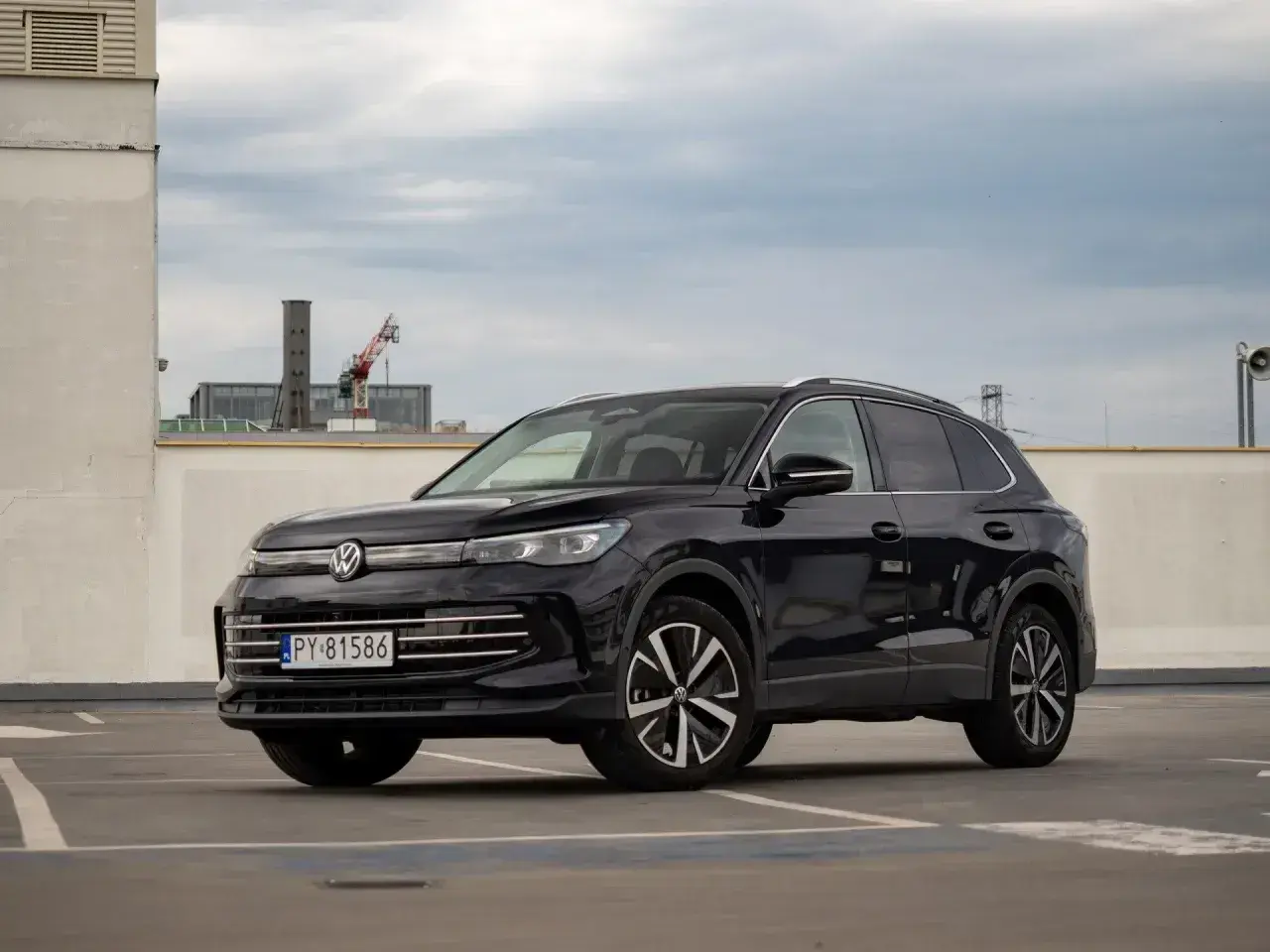 Czarny VW Tiguan Allspace na parkingu pod chmurką. Elegancki SUV z chromowanymi detalami i nowoczesnymi felgami.