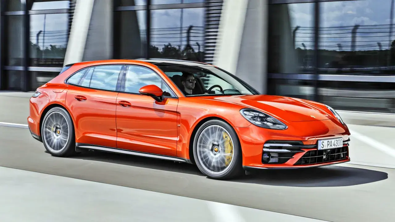 Pomarańczowe porsche 971 Sport Turismo pędzi po drodze, kierowca w okularach przeciwsłonecznych za kierownicą.