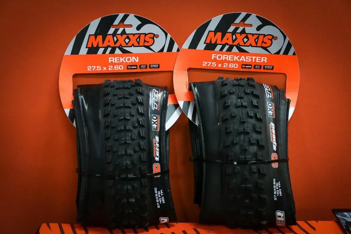 Dwie opony rowerowe Maxxis Rekon i Forekaster 27.5 x 2.60 na pomarańczowym tle.