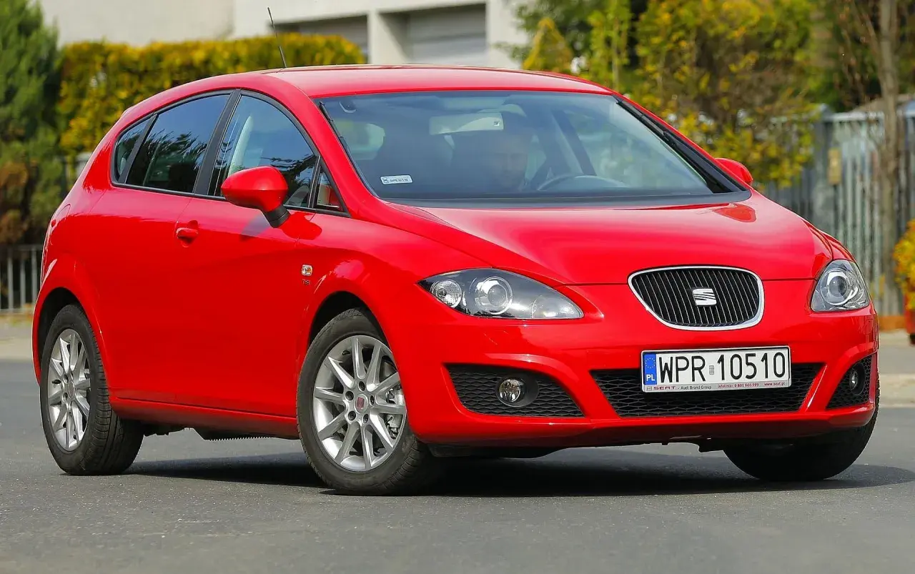 Czerwony Seat Leon 1P1 z polskimi tablicami rejestracyjnymi WPR 10510 na drodze, z kierowcą za kierownicą.