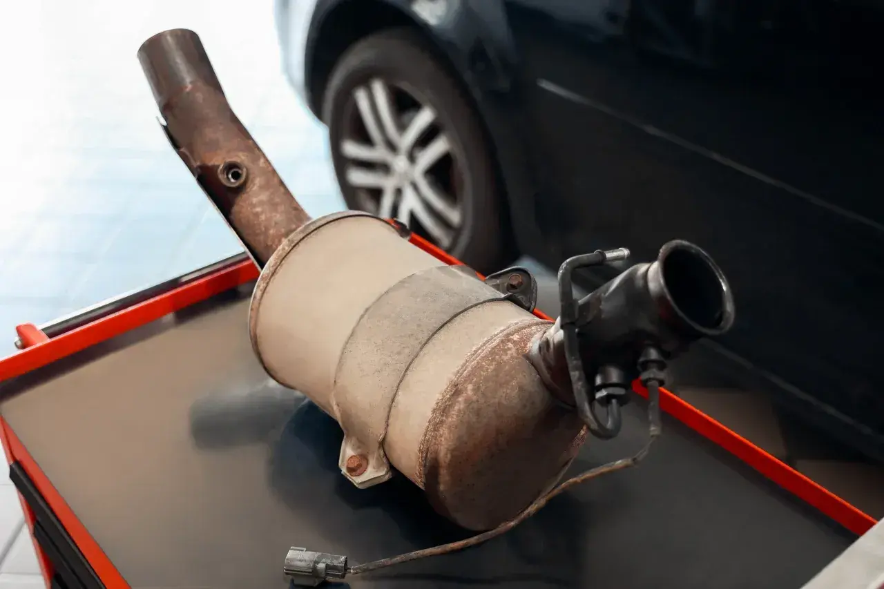 Filtr DPF na stole warsztatowym, z widocznym elementem wydechowym i złączem elektrycznym.