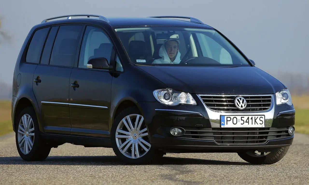 Czarny Volkswagen Touran 1T3 z młodym kierowcą za kierownicą, zaparkowany na drodze.