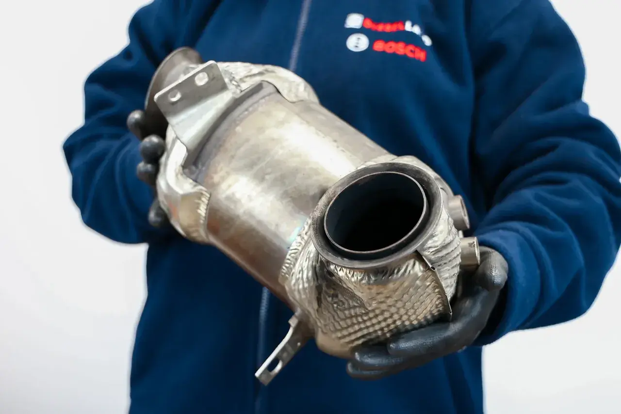 Mechanik w rękawiczkach trzyma katalizator, element układu wydechowego. Rozważasz wyprogramowanie DPF?