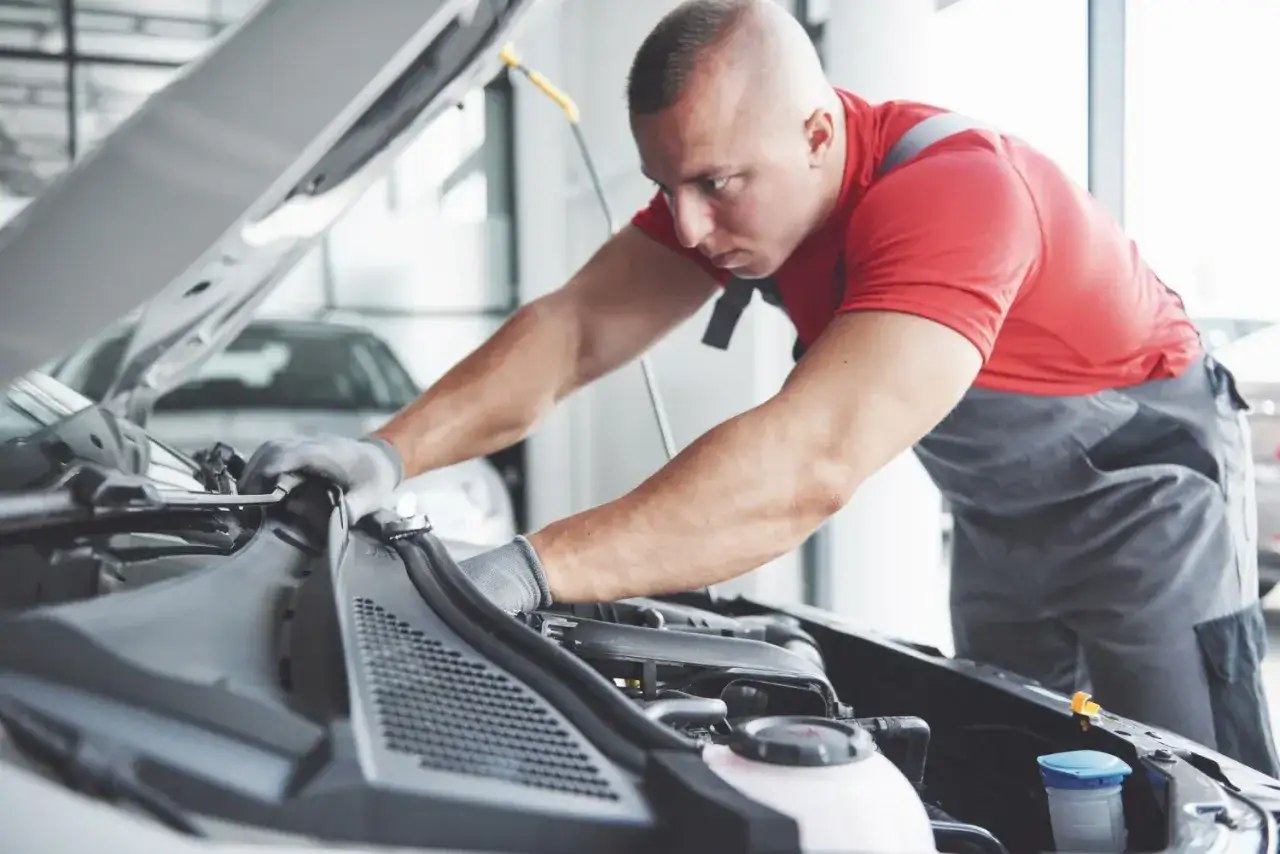 Mechanik w rękawiczkach pracuje przy silniku. Sprawdza, czy wymiana sprężarki klimatyzacji cena jest korzystna.
