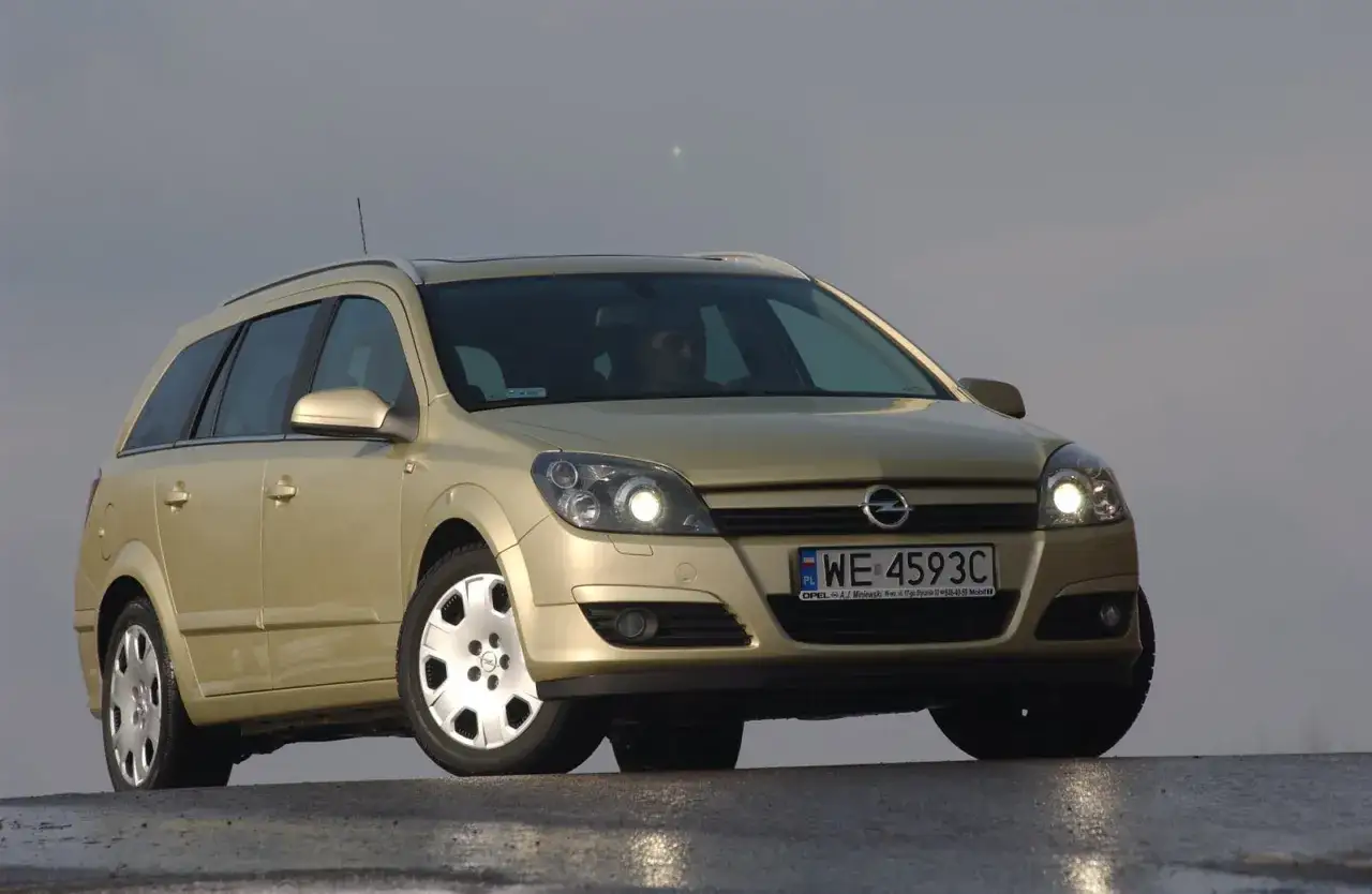 Złoty Opel Astra H kombi z włączonymi światłami. Szukasz informacji, jakie żarówki pasują do tego modelu?