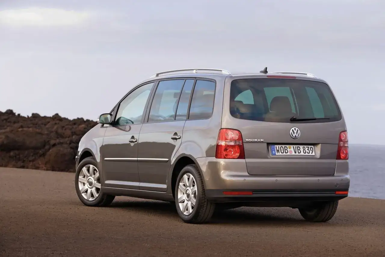 Szary Volkswagen Touran 1T3 zaparkowany na pustkowiu, z widokiem na morze w tle.