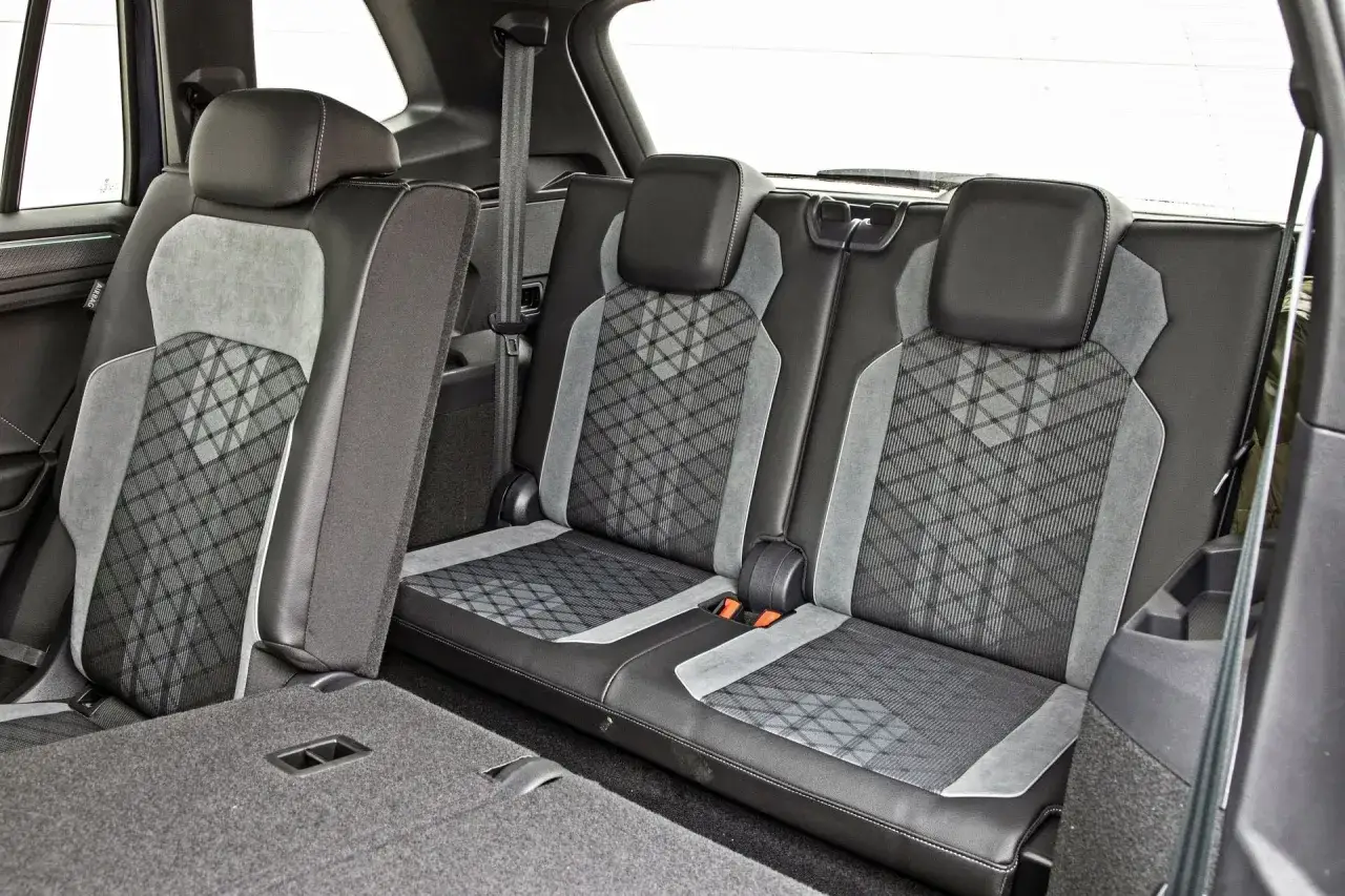 Wnętrze VW Tiguan Allspace: wygodne, tapicerowane fotele z szarym wzorem, pasy bezpieczeństwa i podłoga bagażnika.