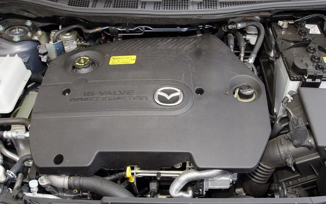 Silnik 16-zaworowy z bezpośrednim wtryskiem w Mazda 5 CR. Widoczny czarny plastikowy kolektor, logo Mazda i elementy układu dolotowego.