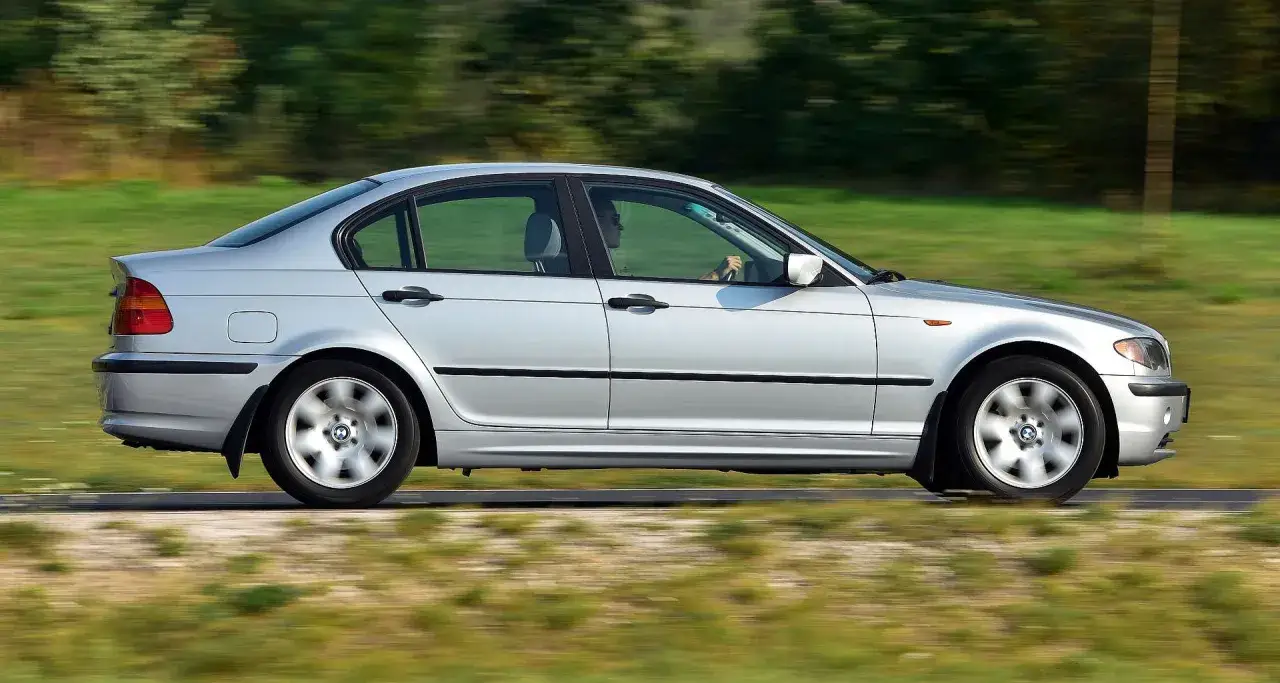 Srebrne BMW E46, rok produkcji 2002, pędzi po drodze, za kierownicą siedzi kierowca.