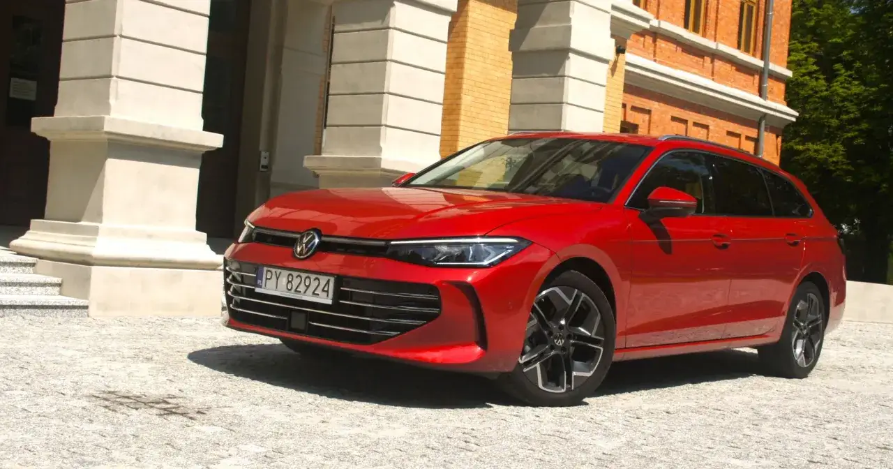 Czerwony Passat B9 kombi zaparkowany przed budynkiem z cegły i kamiennymi kolumnami.