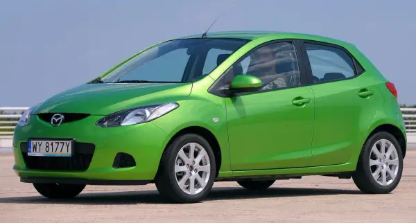 Zielona Mazda 2 DE z polskimi tablicami rejestracyjnymi WY 8177Y stoi na zewnątrz.