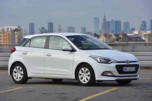 Biały Hyundai i20 zaparkowany na parkingu z widokiem na miasto w tle.