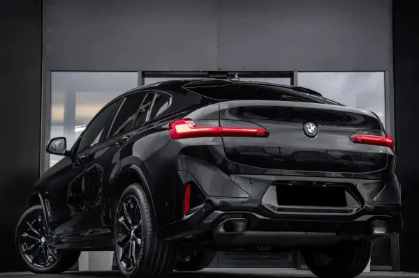 Elegancki, czarny BMW X4 G02 z przyciemnianymi szybami i sportowymi felgami prezentuje się imponująco na tle nowoczesnej, szarej ściany.