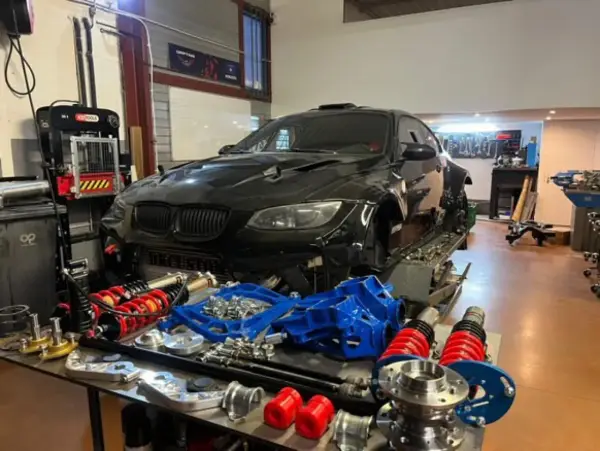 Warsztat z czarnym BMW E92, częściami zawieszenia i narzędziami. Lata produkcji tego modelu to 2006-2013.