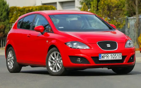 Czerwony Seat Leon 1P1 z polskimi tablicami rejestracyjnymi WPR 10510 na drodze, z kierowcą za kierownicą.