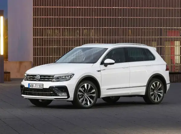 Biały Volkswagen Tiguan 5N z przyciemnianymi szybami i chromowanymi listwami, zaparkowany przed nowoczesnym budynkiem.